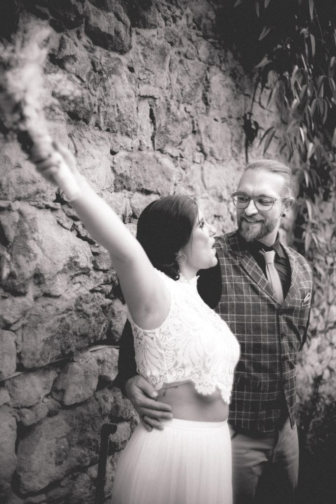 Hochzeitspaar von Nina Hübner Hochzeitsplanung Göttingen Paar in blütenweißer Brautausstattung vor einer steinernen Wand, lächelnd und verliebt.